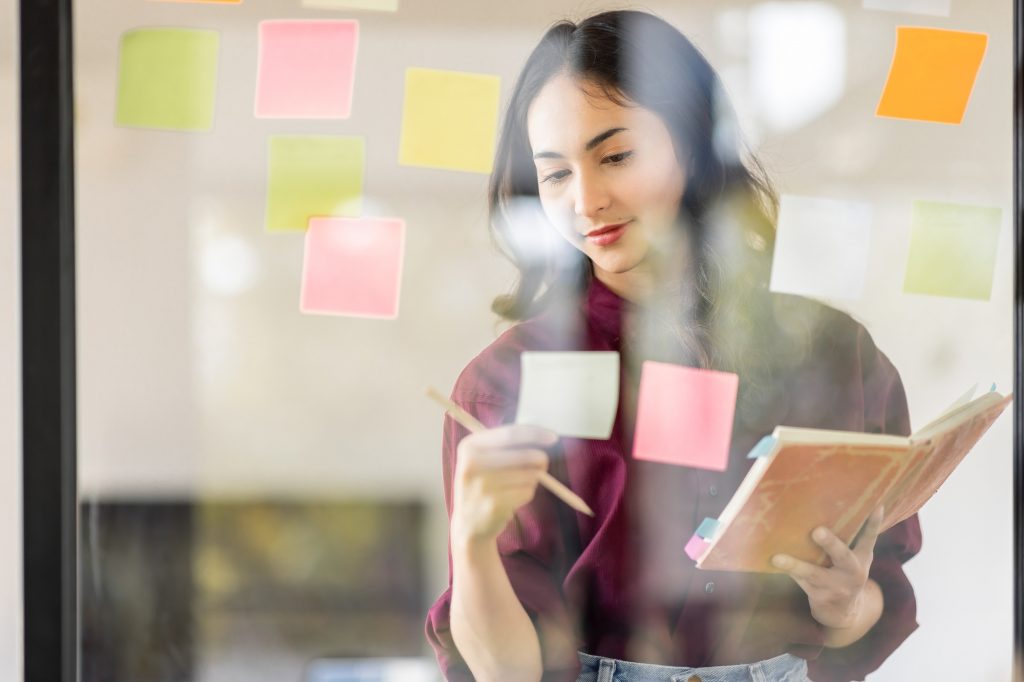 Business female employee with many conflicting priorities arranging sticky notes commenting and